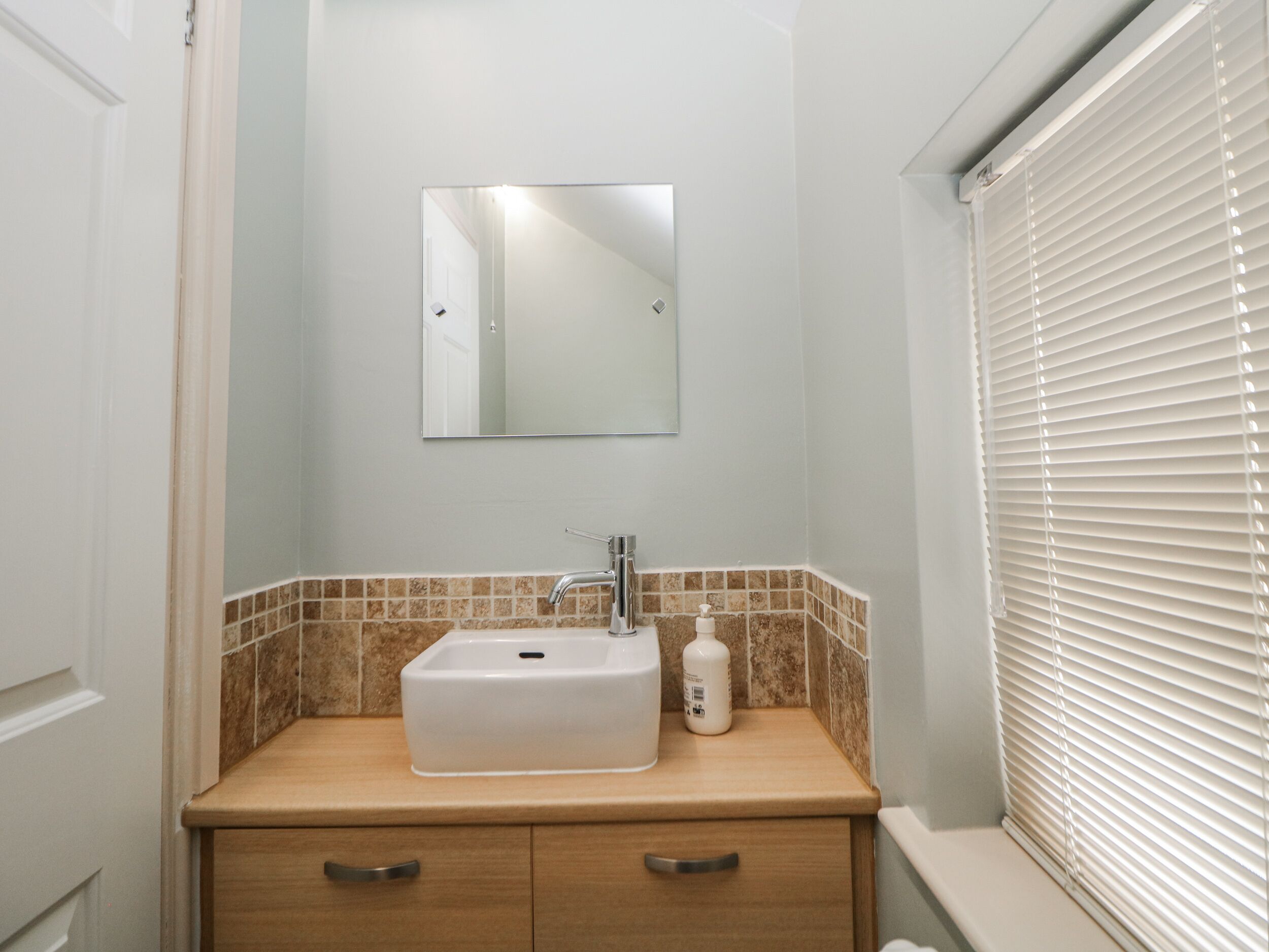 Une salle de bain avec un lavabo blanc, un miroir et une fenêtre avec des stores.