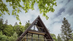 A modern house with a large glass facade, a stone patio, and a wooden deck. - HOUSE28 - Modern A-Frame in the woods (Grattersdorf)