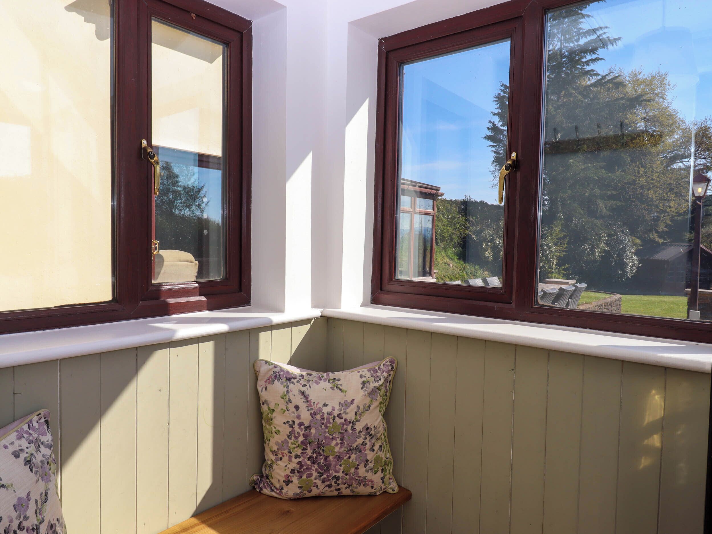 A corner with two windows, a bench, and a cushion.