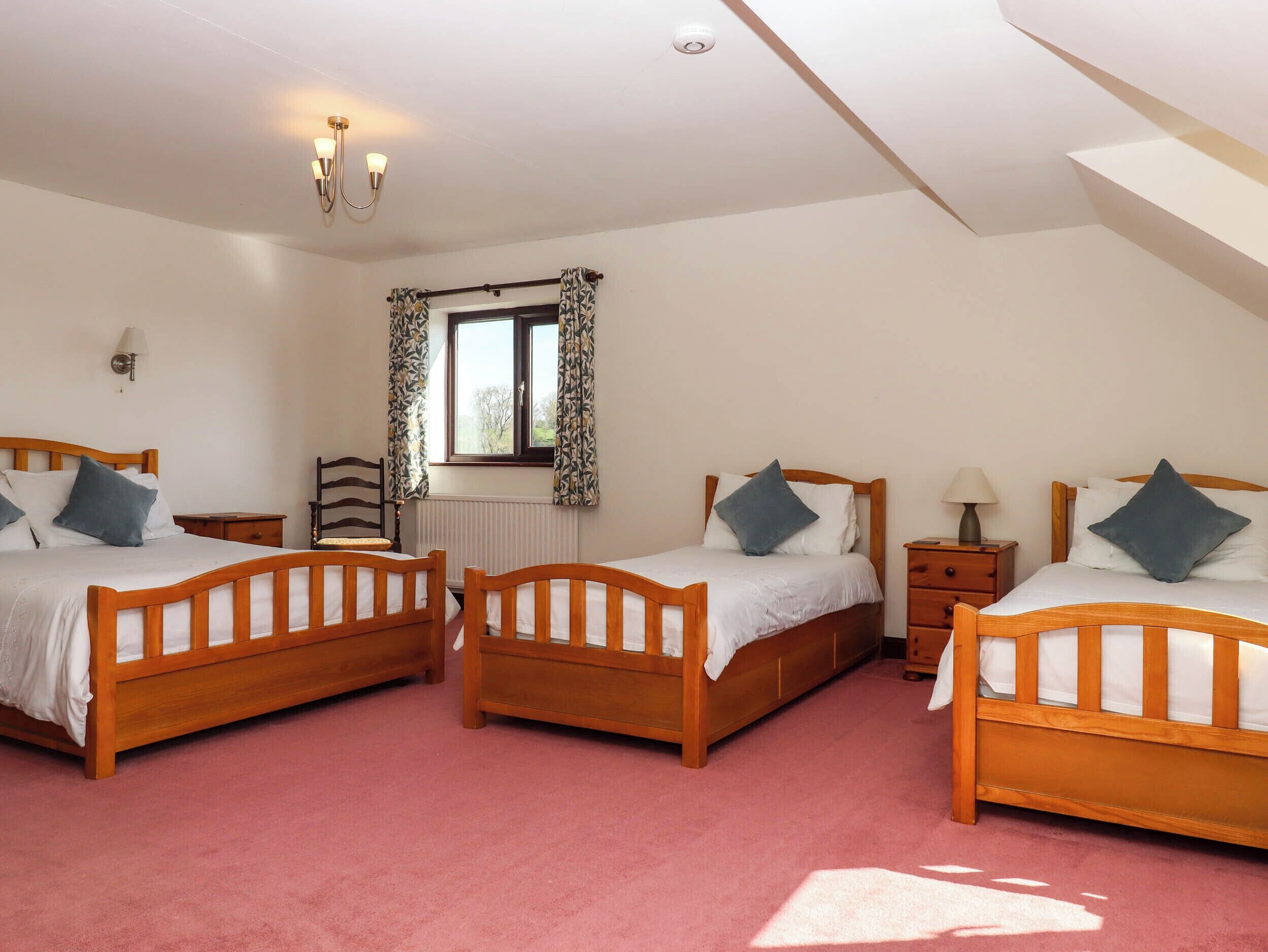 Une chambre à coucher avec trois lits en bois, une fenêtre avec des rideaux à motifs, un radiateur et une lampe fixée au mur.