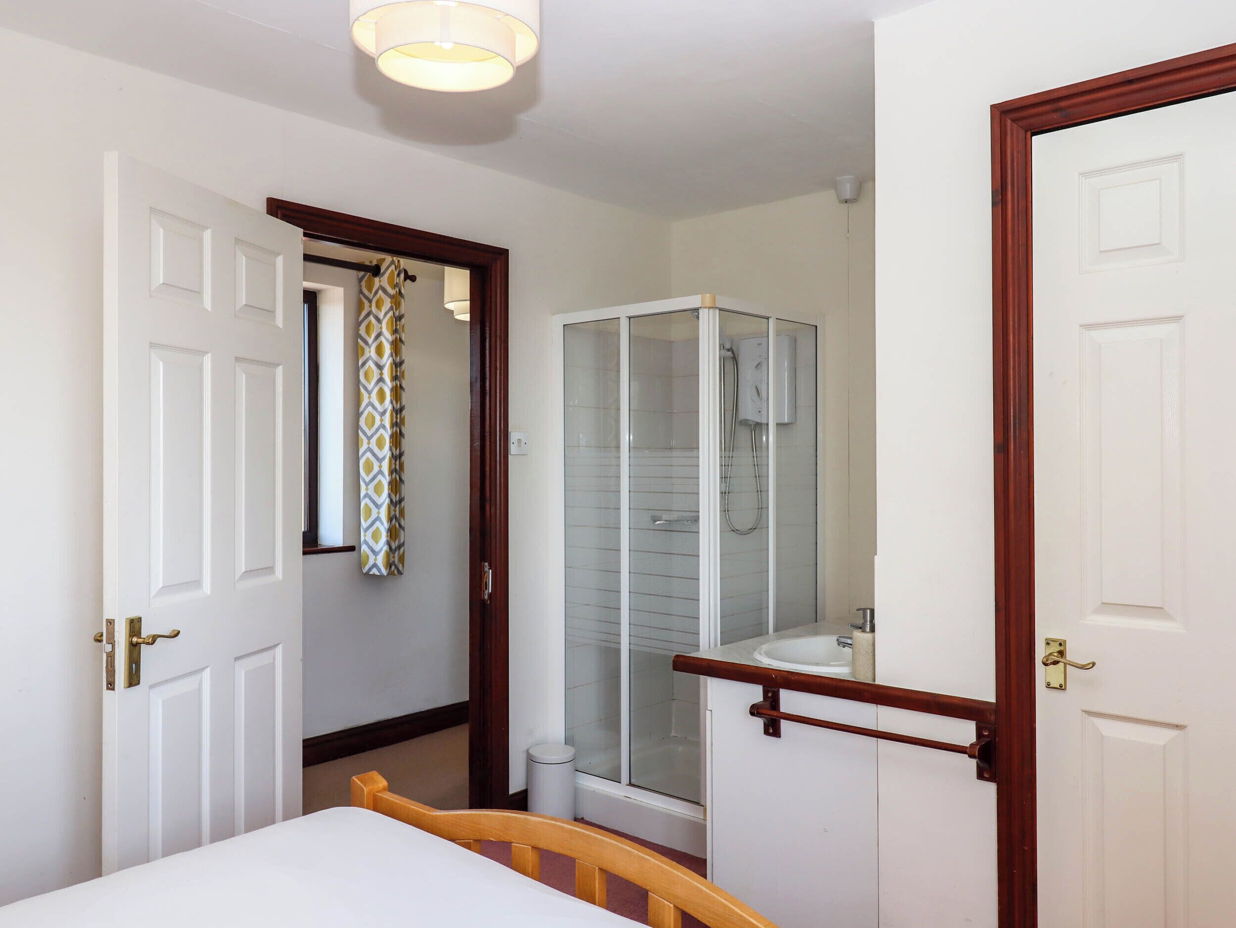 A hotel room with a bed, a bathroom with a glass shower enclosure, and a white sink.