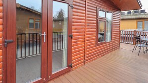 A wooden cabin with large sliding glass doors, a deck with outdoor furniture, and a visible neighboring building. - Brightwater Lodge (Windermere)