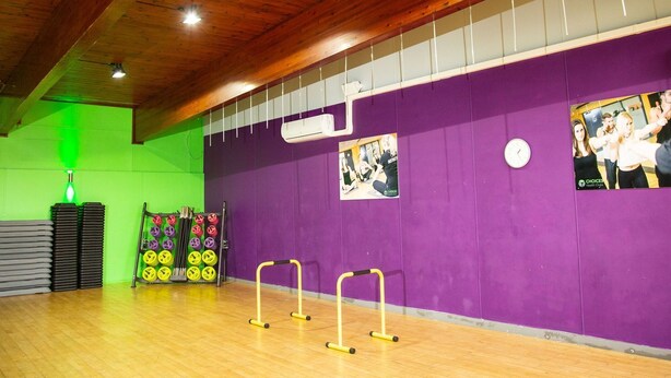 Une salle de sport aux murs violets, avec des poutres en bois et du matériel d’exercice.
