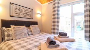 A hotel room with a checkered bedspread, two pillows with 'ORIGINAL' labels, a framed quote on the wall, and a view through the window. - Brightwater Lodge (Windermere)