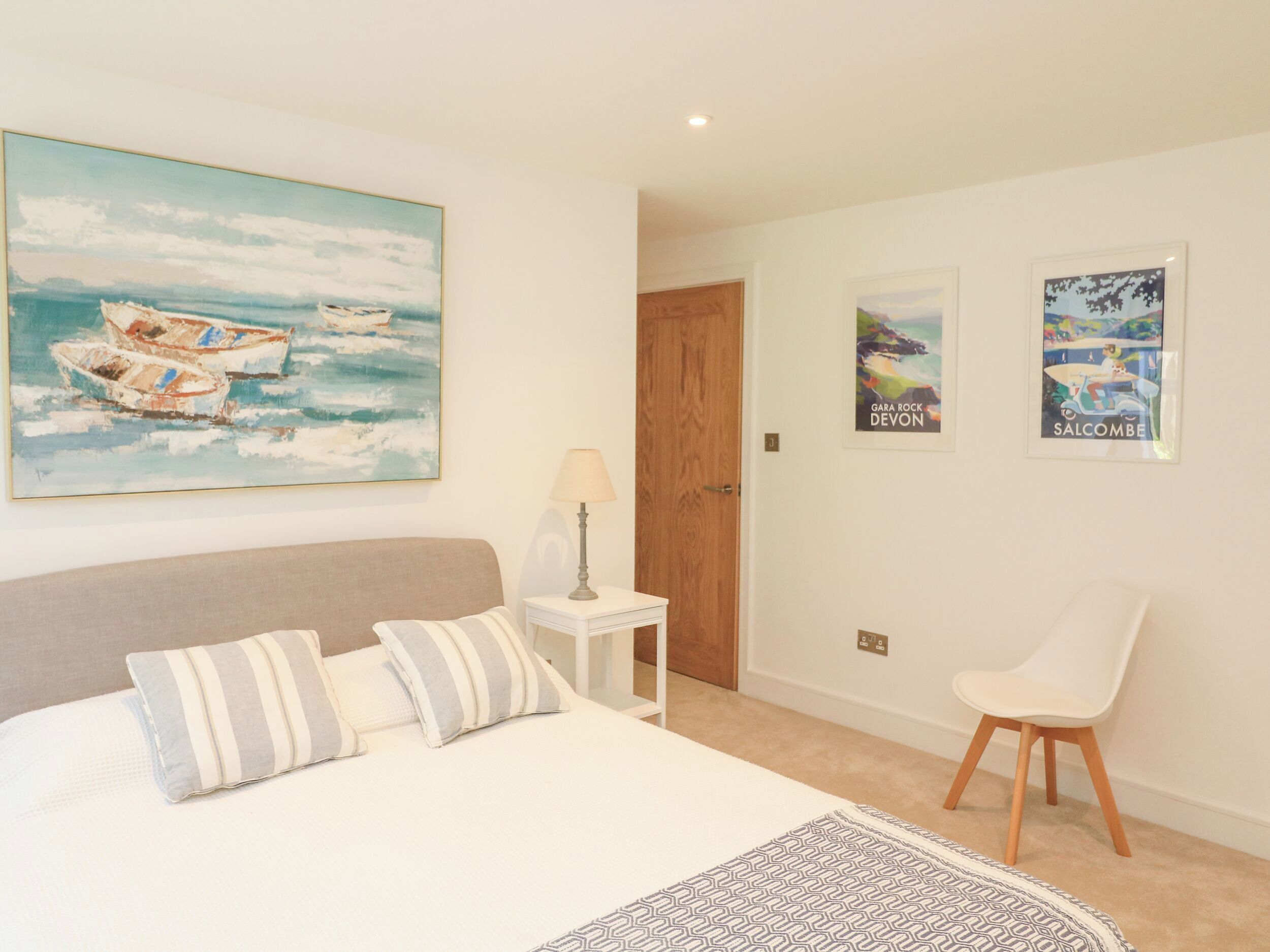 Un dormitorio con una cama, almohadas, una mesita de noche, una lámpara, una silla y decoración en la pared que muestra barcos y una scooter.
