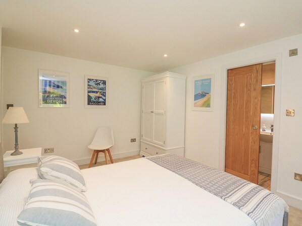 A bedroom with a bed, a nightstand, a lamp, a chair, a wardrobe, and a door leading to a bathroom.