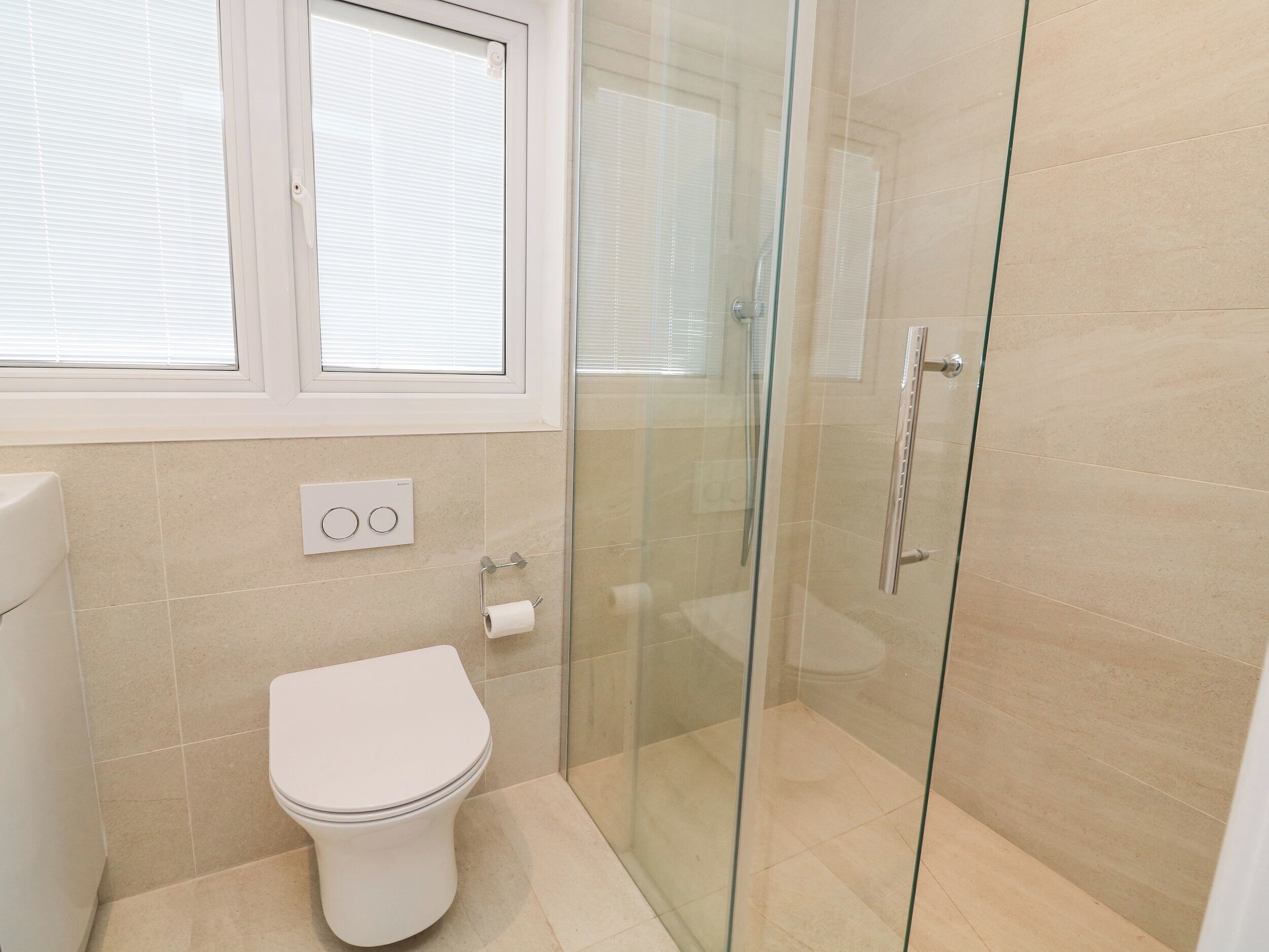 A bathroom with a toilet, a glass shower enclosure, and a window with blinds.