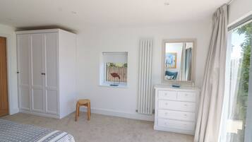 A bedroom with a bed, a wardrobe, a dresser, a small stool, a window with curtains, and a framed picture on the wall.