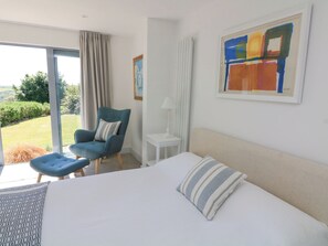 Un dormitorio con una cama grande, un sillón azul, una mesita y un cuadro en la pared.