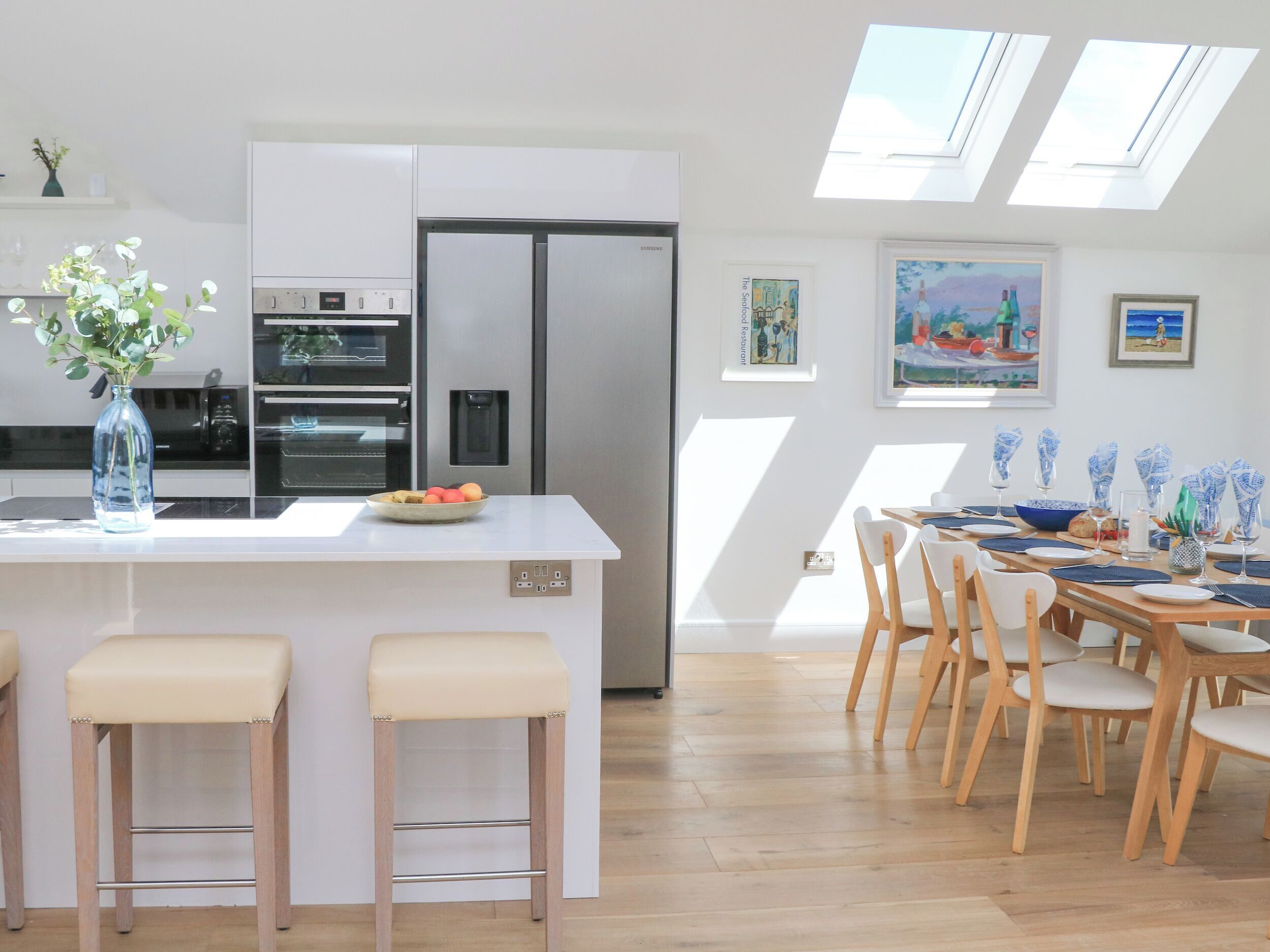 Una cocina moderna con una isla central, taburetes de bar y un comedor con sillas de madera y una mesa dispuesta para seis personas.