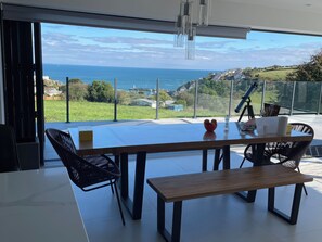 Ein moderner Essbereich mit großem Tisch, Stühlen und einer Bank. Er verfügt über ein Glasgeländer mit Panoramablick auf den Ozean.