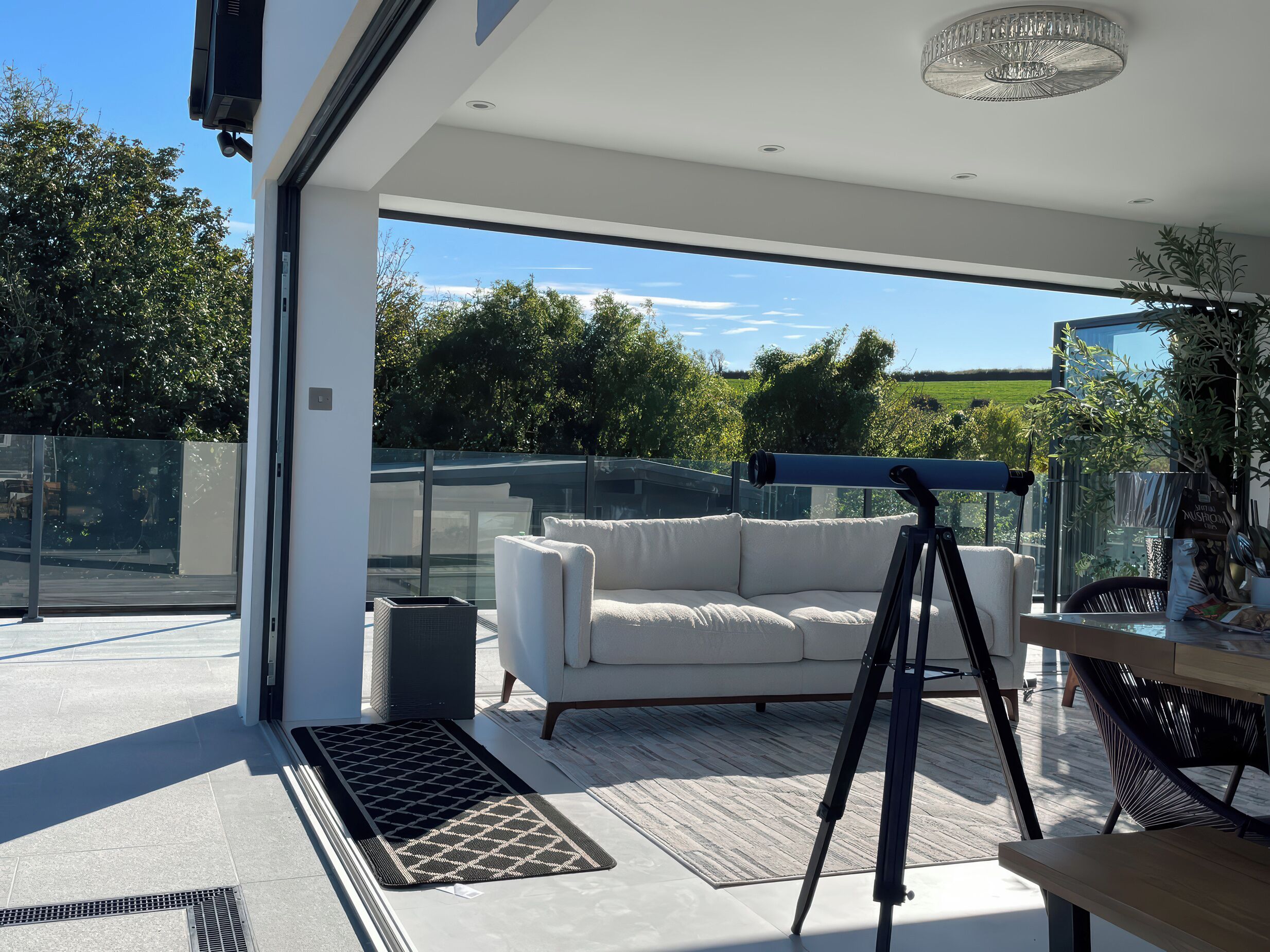 Un espacio exterior moderno con un sofá blanco, un telescopio y una mesa de comedor.