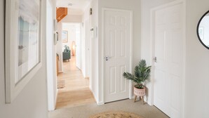 A hallway with white doors, a woven ceiling light fixture, and a potted plant. - The Palms (Pwllheli)