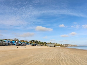 A beach with rows of colorful beach huts and a sandy beach. - The Palms (Pwllheli)