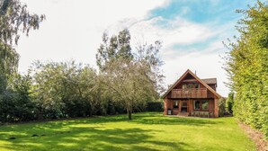Ein zweistöckiges Holzhaus mit Balkon, umgeben von einem gepflegten Rasen und Bäumen.