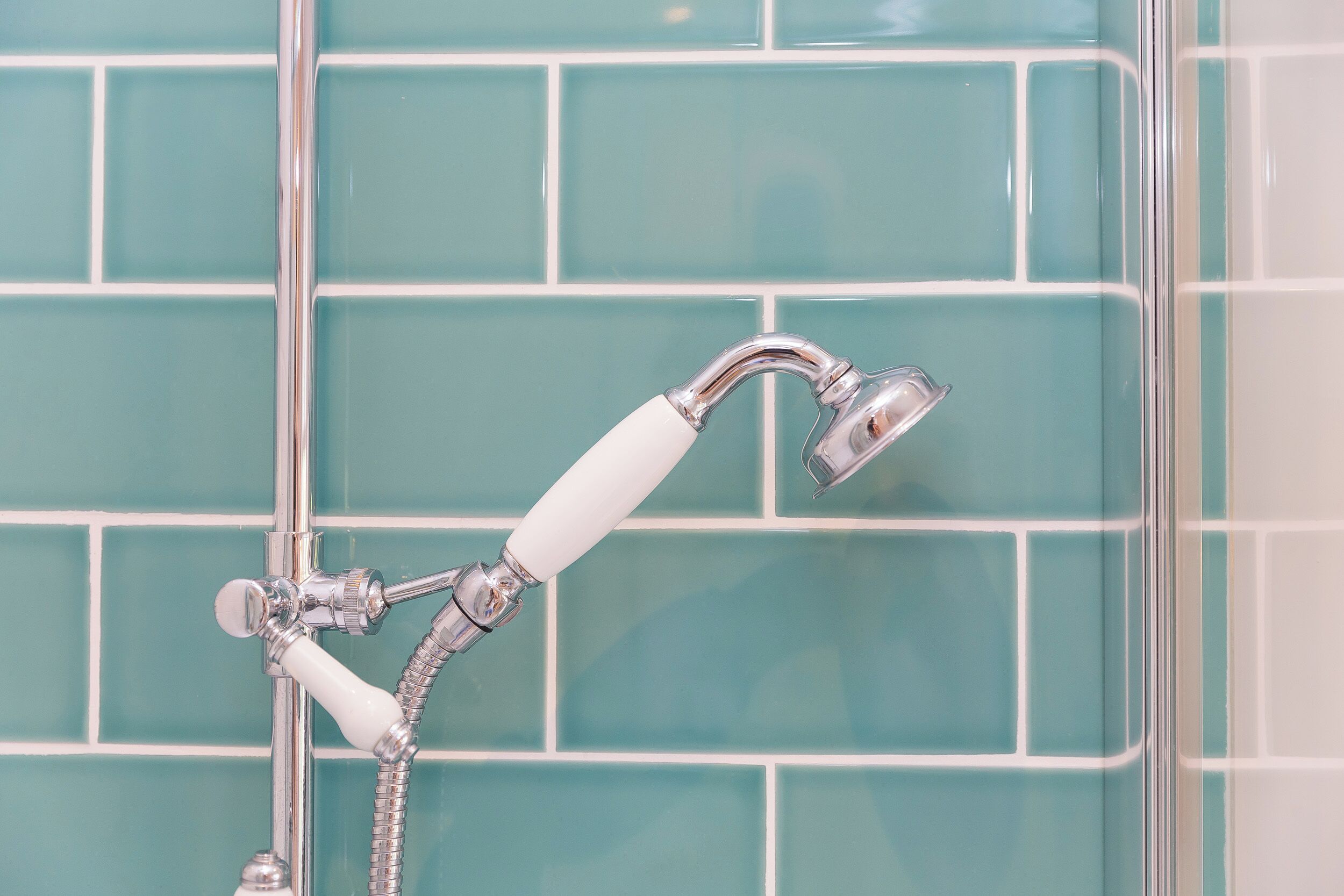 Une salle de bain avec un pommeau de douche fixé au mur et un flexible de douche amovible, le tout installé sur un mur carrelé.