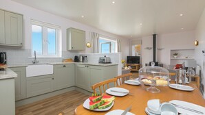 A modern kitchen with grey cabinets, a wooden dining table set with plates, a coffee maker, and a toaster. - Rowena (Helston)