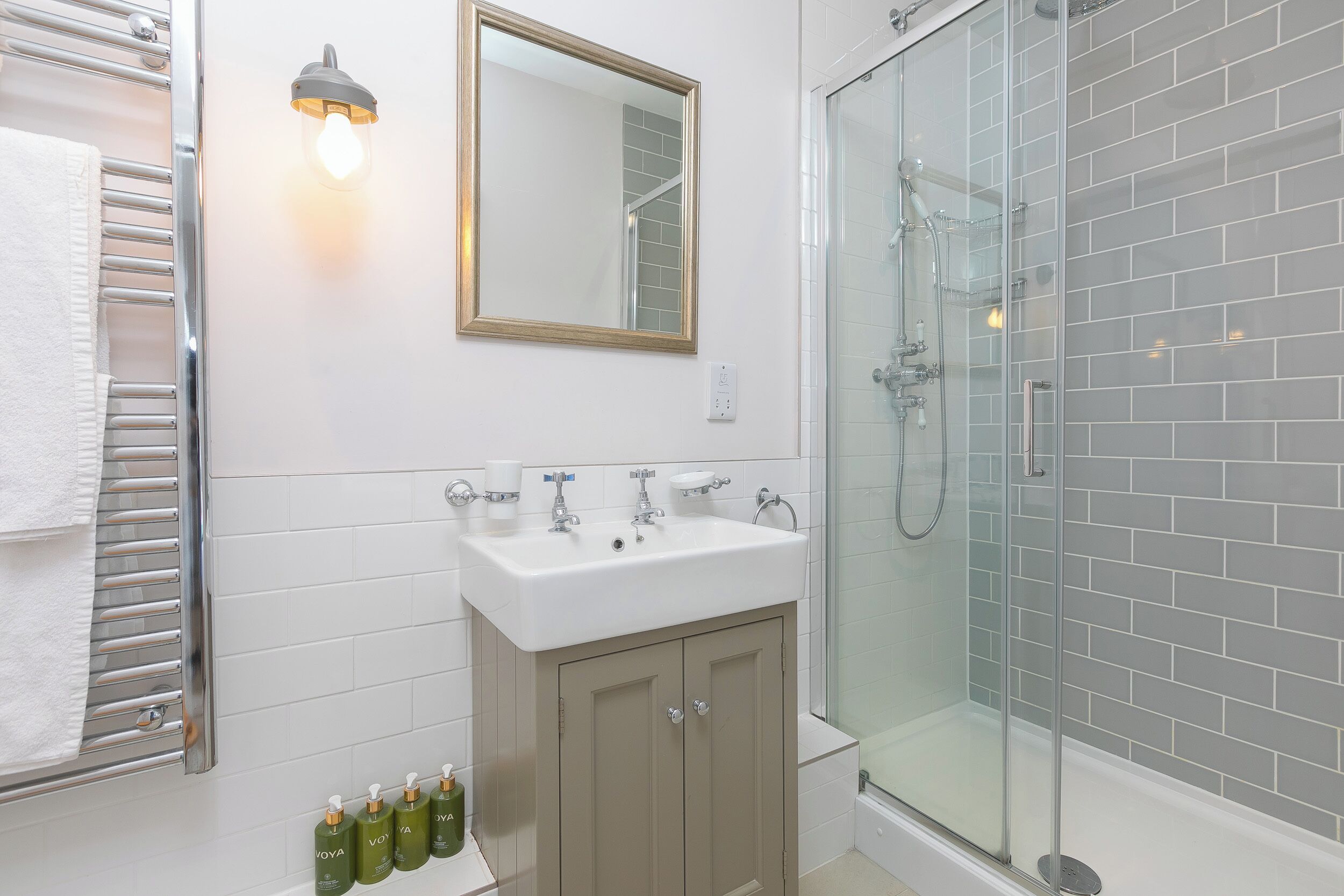 Une salle de bain avec une douche à parois de verre, un lavabo blanc avec un miroir au-dessus et un porte-serviettes.