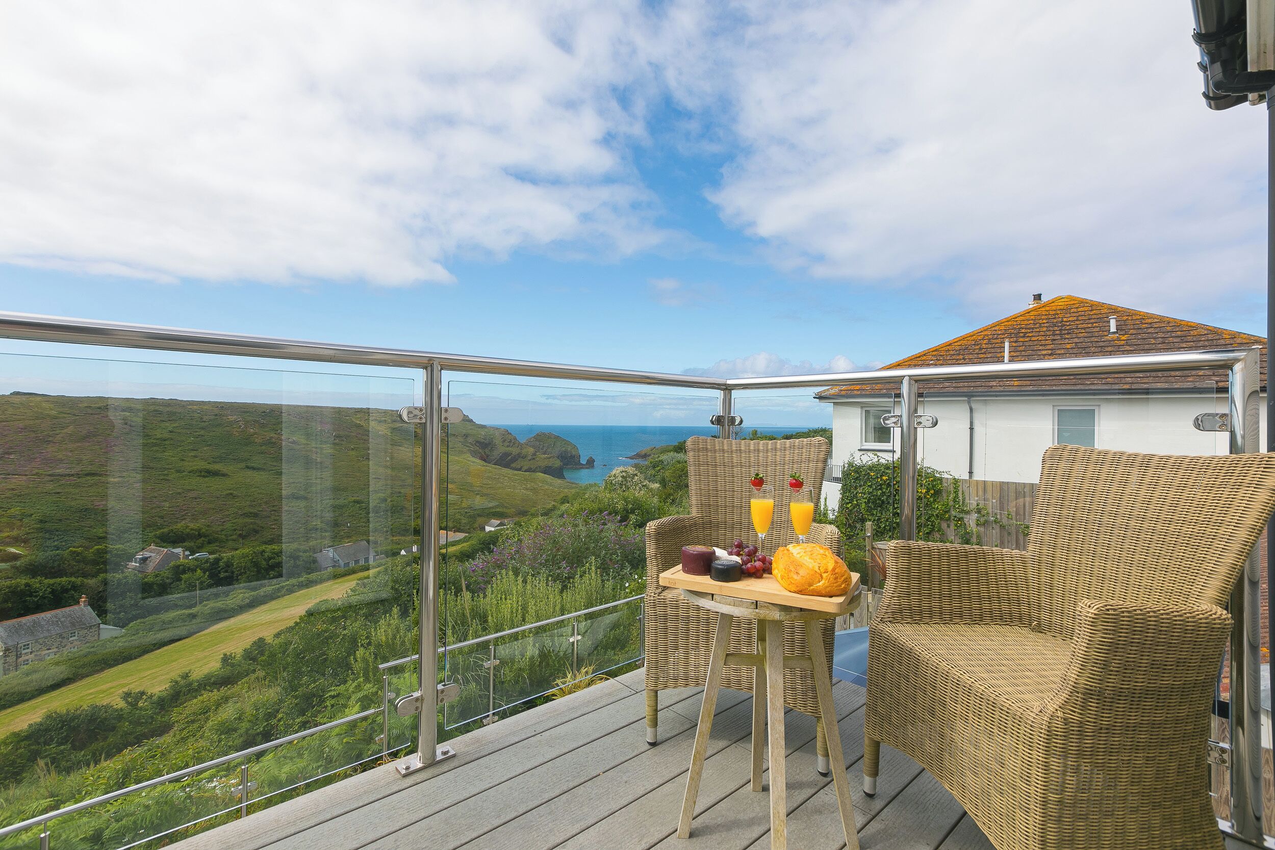 Un balcone con una sedia e un tavolino in vimini, con vista su un paesaggio suggestivo e il mare.