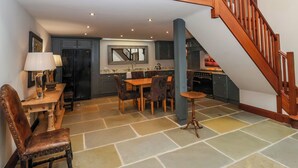 A spacious kitchen with a dining area, a wooden staircase, and a stone-tiled floor. - The Barn (Knaresborough)