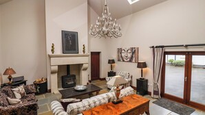 A spacious living room with a fireplace, a chandelier, and a view through a glass door. - The Barn (Knaresborough)