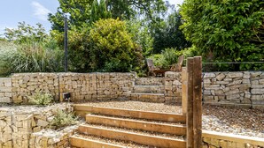 Una escalera de piedra conduce a una terraza de madera rodeada por un muro de piedra, con un banco y una silla a la vista en el fondo.