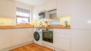 Una cocina moderna con armarios blancos, horno empotrado, microondas y lavadora.