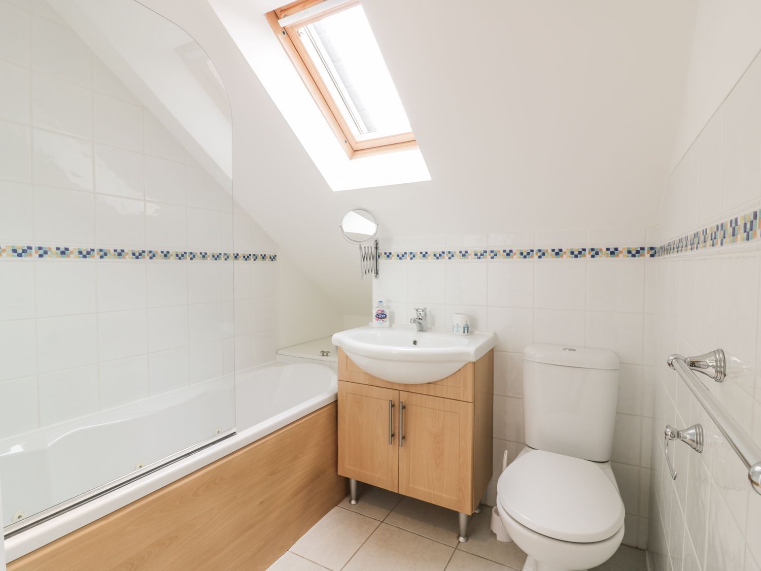 A modern bathroom with a skylight, a bathtub, a toilet, and a sink with wooden cabinets.
