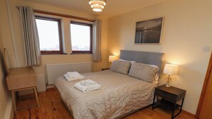 Una camera da letto con un letto, due abat-jour, un termosifone, una finestra con tende e un quadro appeso al muro.