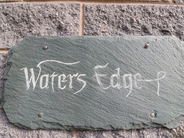 Une plaque d’ardoise portant l’inscription « Waters Edge » est fixée à un mur de pierre.