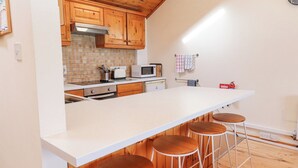 Una cucina con mobili in legno, un piano di lavoro bianco, un forno a microonde, un tostapane e tre sgabelli.
