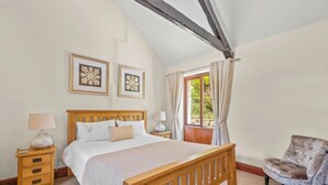 Un dormitorio con una cama de madera, una mesita de noche con una lámpara, una silla y dos cuadros en la pared.
