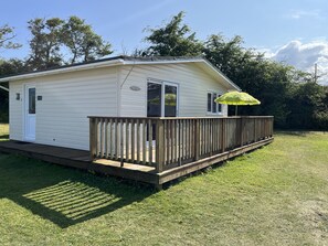 A small, single-story mobile home with a wooden deck and a covered patio area. - Chalet 3 Wipeout (Hayle)