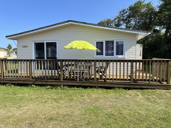A single-story mobile home with a fenced deck, a patio table, and a bright yellow umbrella. - Chalet 3 Wipeout (Hayle)
