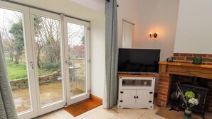 Una sala de estar con televisión sobre un mueble de madera, chimenea y puerta corrediza de vidrio que da a un jardín.