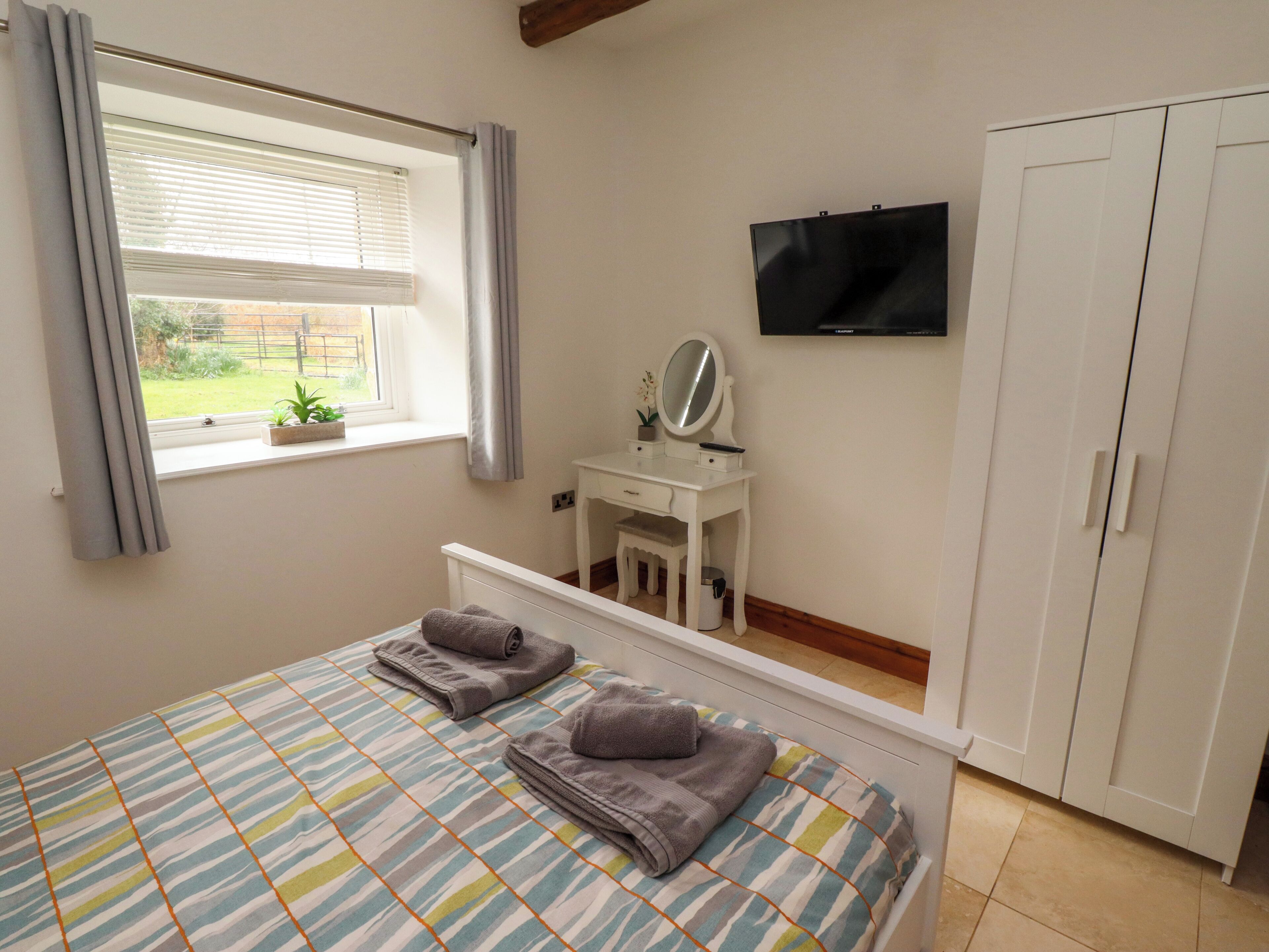 A bedroom with a bed, a bedside table with a mirror, a TV mounted on the wall, and a wardrobe.