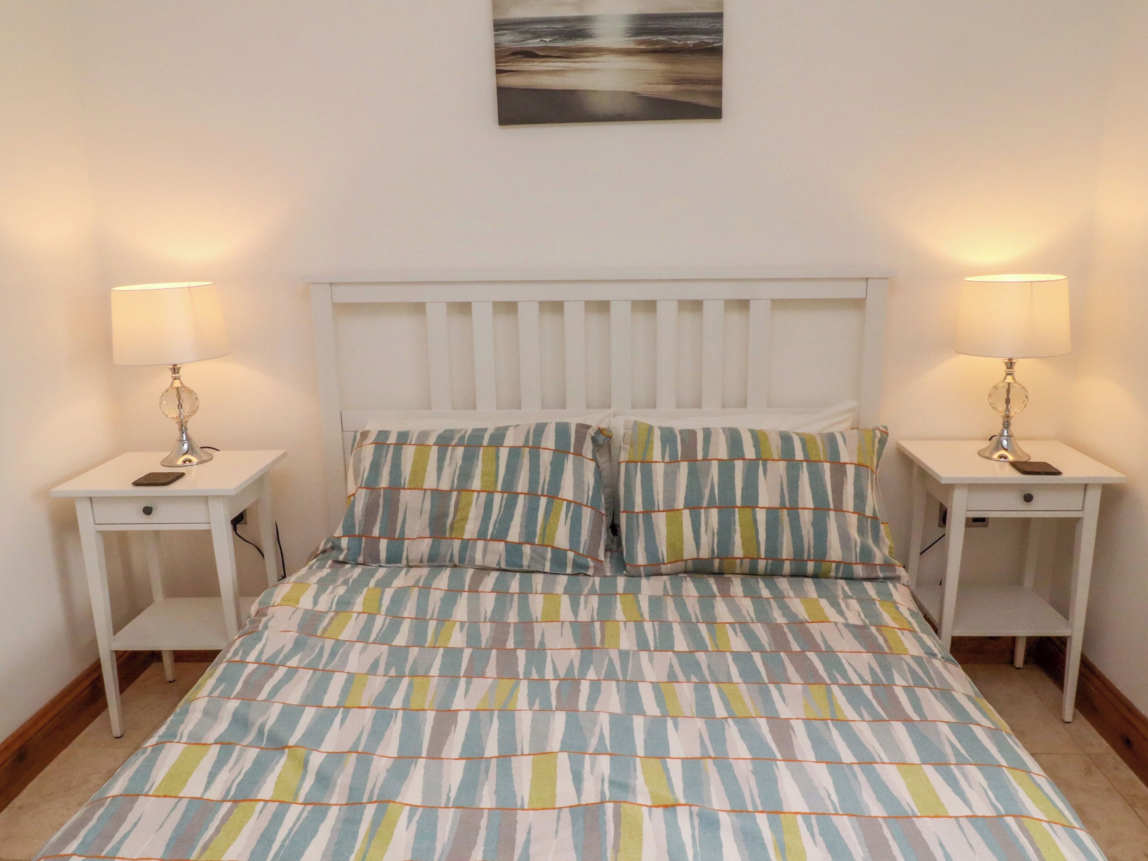 Ein Schlafzimmer mit einem Bett, zwei Nachttischen, zwei Lampen und einem Wandbild.