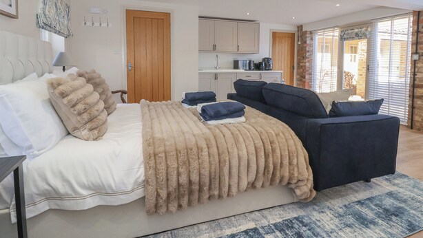 Een slaapkamer met een bed, een slaapbank, een houten deur, een keukenhoek en een groot raam met zonwering.