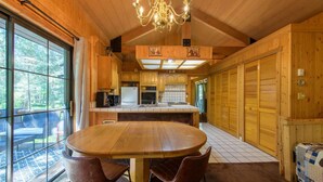 Interior de una cabaña de madera con comedor, cocina y ventanas amplias.