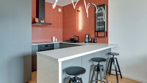 A modern kitchen with a central island, bar stools, and a unique ceiling light fixture. - RentPlanet - Apartamenty Żurawie (Gdansk)