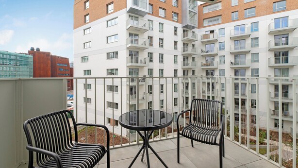 A balcony with two chairs and a table, overlooking a modern apartment building with multiple balconies. - RentPlanet - Apartamenty Żurawie (Gdansk)