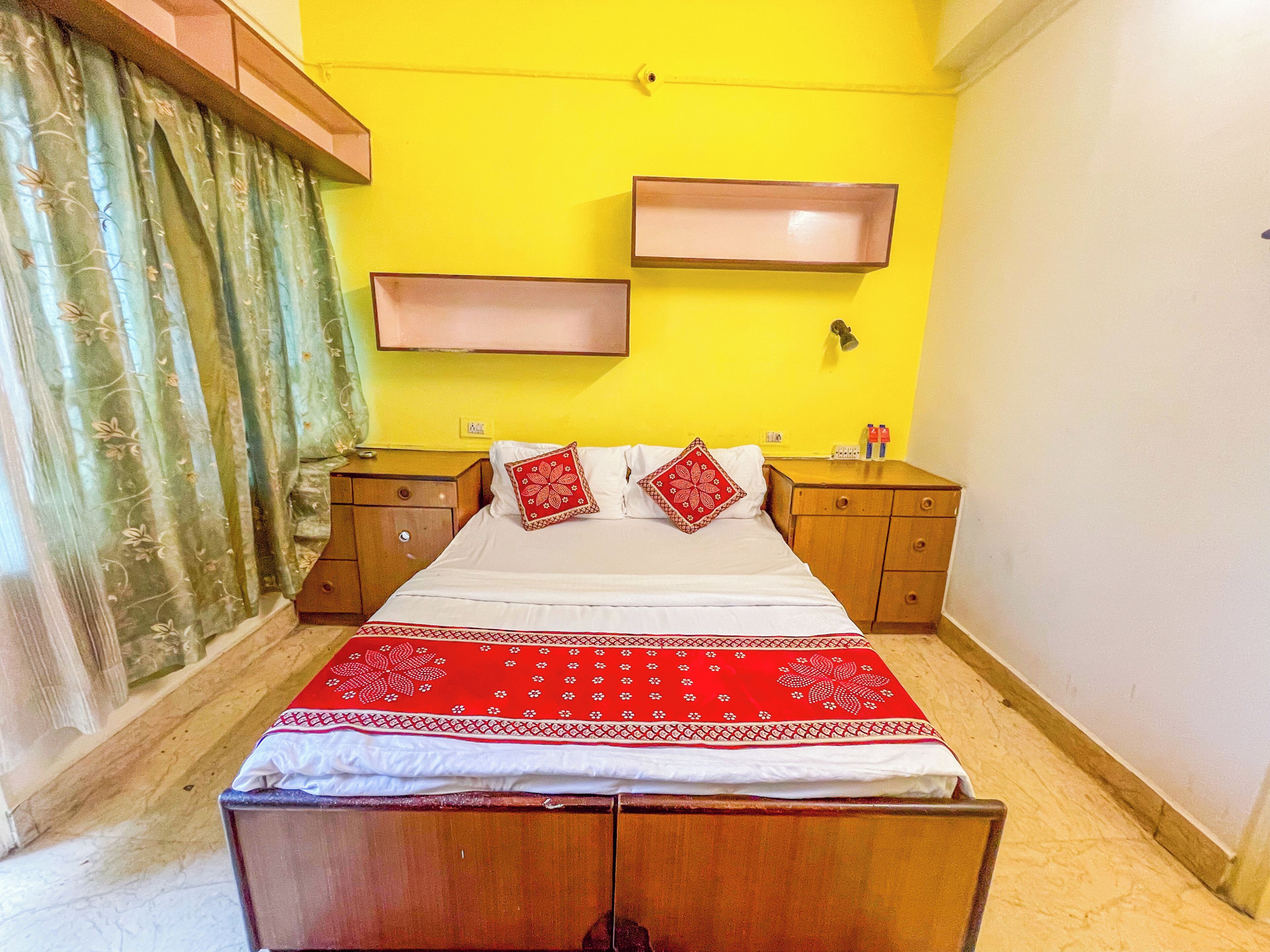 A bedroom with a bed, two nightstands, a red and white patterned bedspread, a wooden headboard, and a yellow wall.