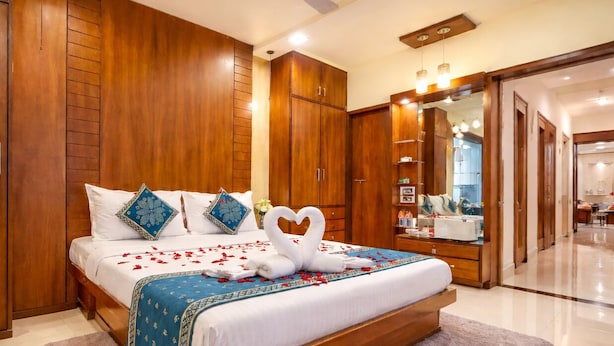 Une chambre d’hôtel avec un grand lit, une armoire en bois, un ventilateur de plafond et une salle de bain visible à travers une porte ouverte.