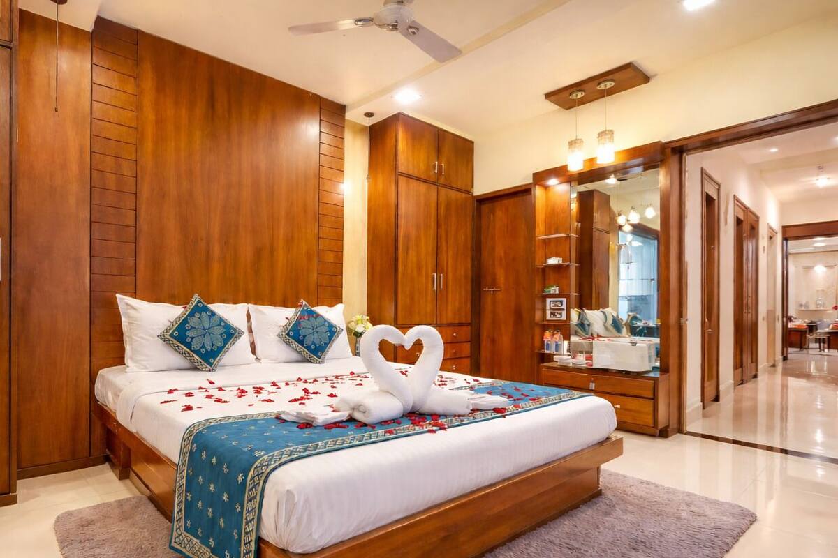 A hotel room with a large bed, wooden wardrobe, a ceiling fan, and a bathroom visible through an open door.
