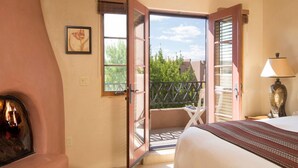 Un dormitorio con cama, una silla, una lámpara, una puerta abierta que da a un balcón y un cuadro en la pared.