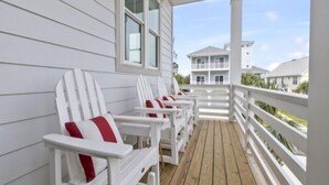 A covered porch with white Adirondack chairs and a wooden deck. - A Treasure To Sea 4 Bedroom Villa (Carolina Beach)