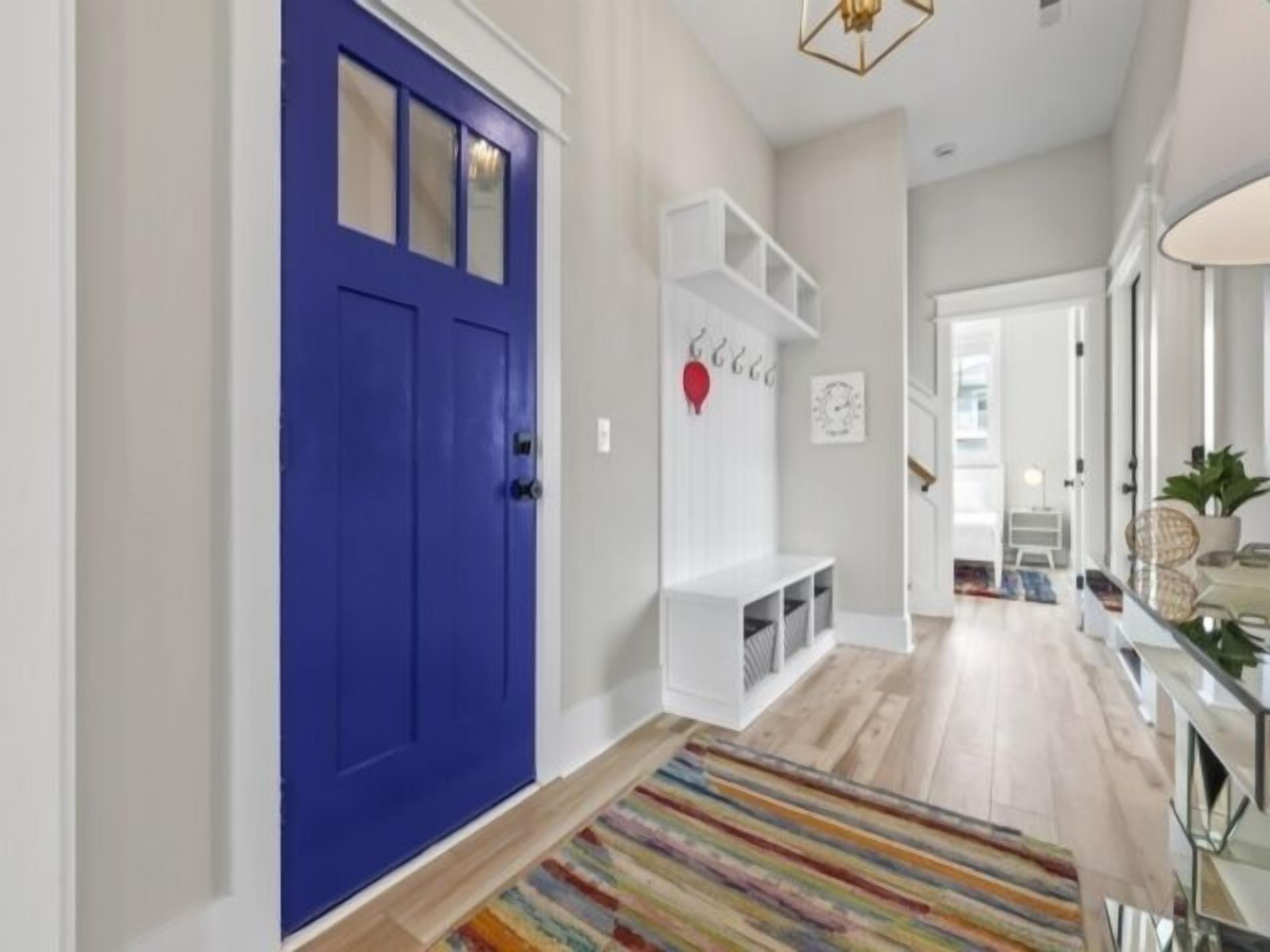 A hallway with a blue door, white shelving, a colorful striped rug, and a staircase leading to another room.