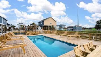 A wooden deck with a pool and lounge chairs, surrounded by houses and a tall communication tower.