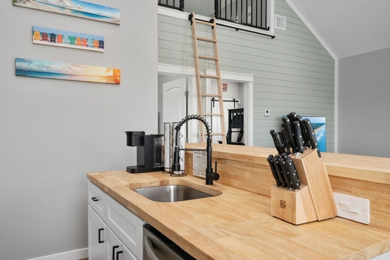 Et køkken med en træbordplade, en stålvask, en kaffemaskine og et knivblok.