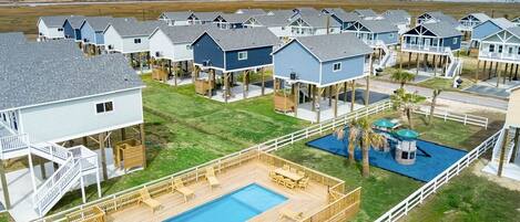 A coastal residential area with elevated houses, a swimming pool, and a playground.